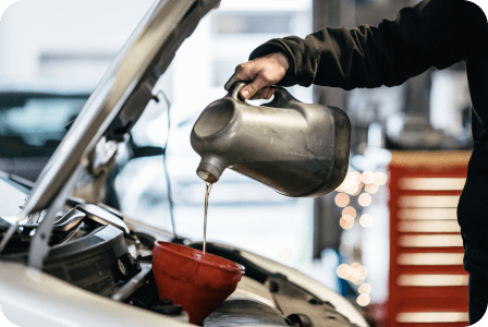 Repair shop with mechanic pouring oil into car